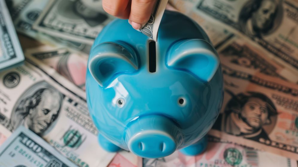 A blue piggy bank sitting on a pile of cash.