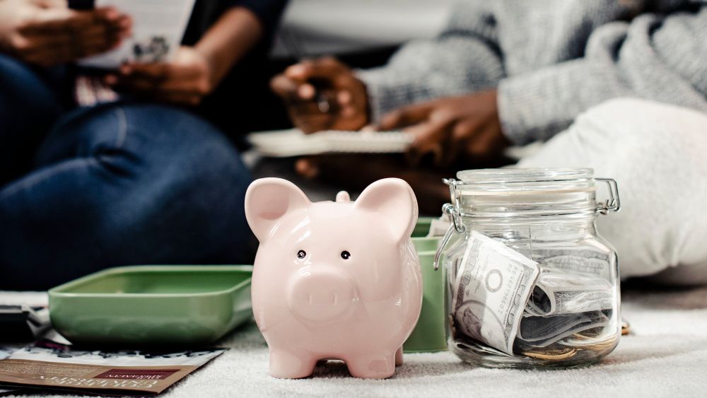 A piggy bank beside a jar of cash.