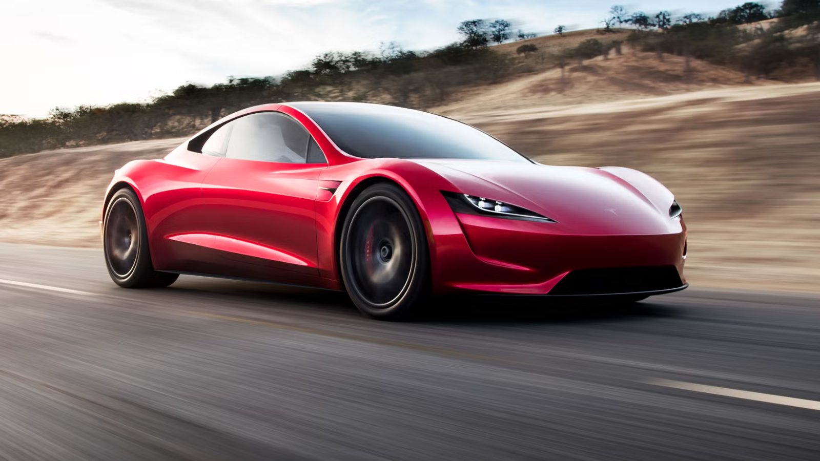 A red Tesla Roadster on an open road, with dry hills behind it.