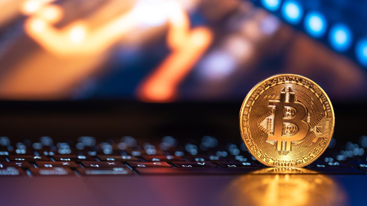 A gold bitcoin coin standing on a laptop keyboard.