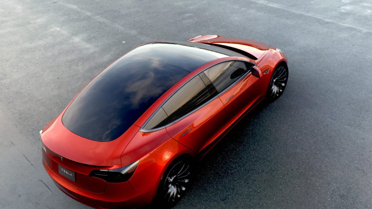 A red Tesla Model 3 seen from above, parked on gray pavement.