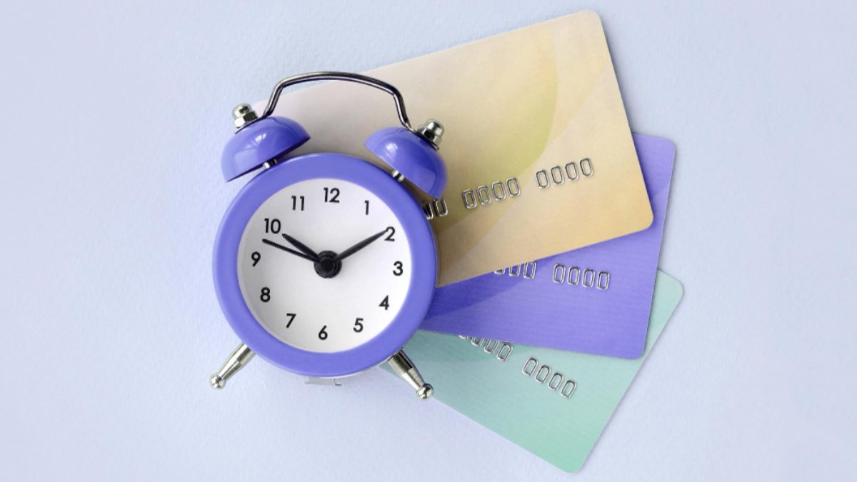A purple alarm clock resting on three fanned-out credit cards.