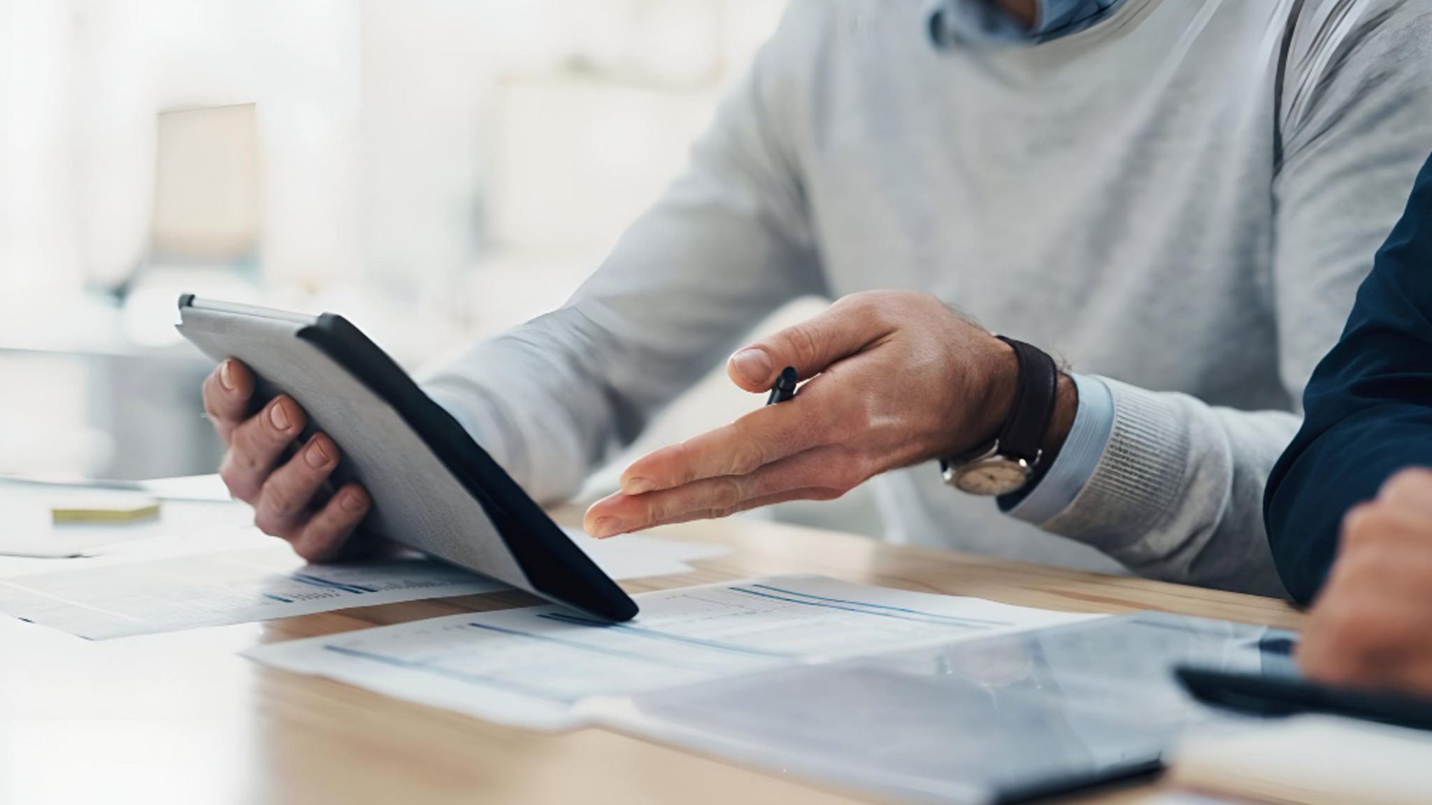 Two people at a desk reviewing account statements on paper and a tablet.