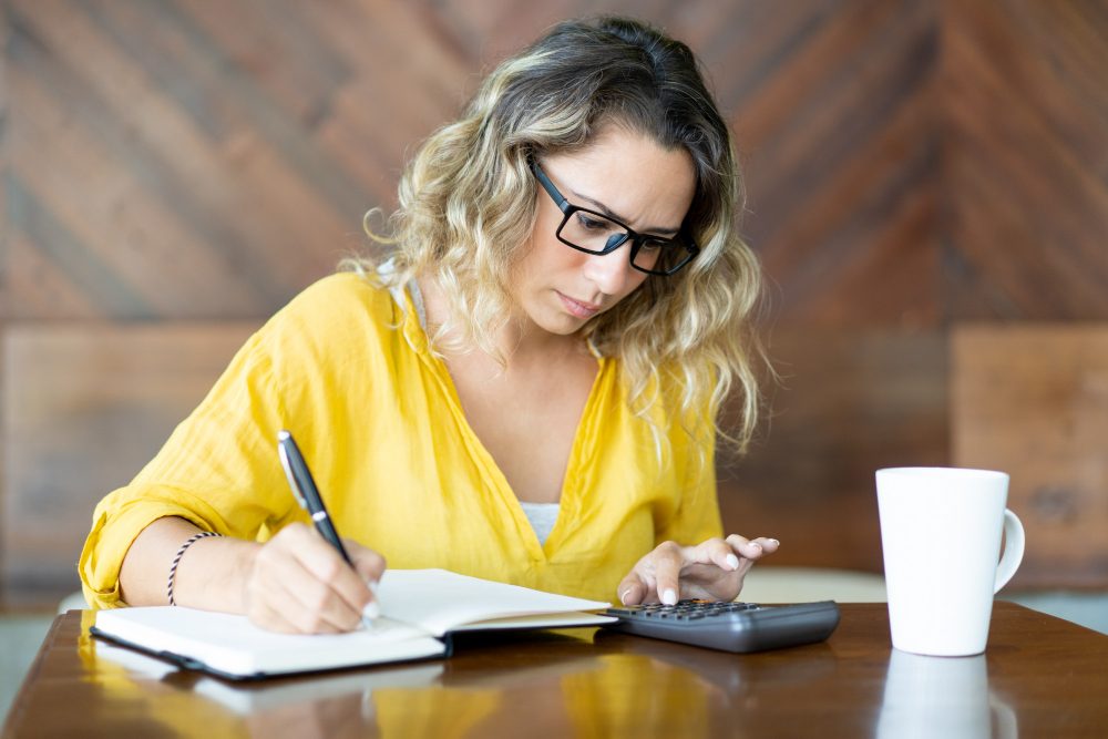 A person at a desk working through figures in a notebook with a calculator.